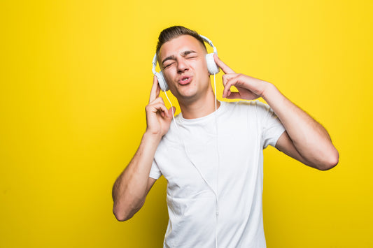 pretty handsome young man in white t-shirt listen music with his new earphones isolated on yellow wall