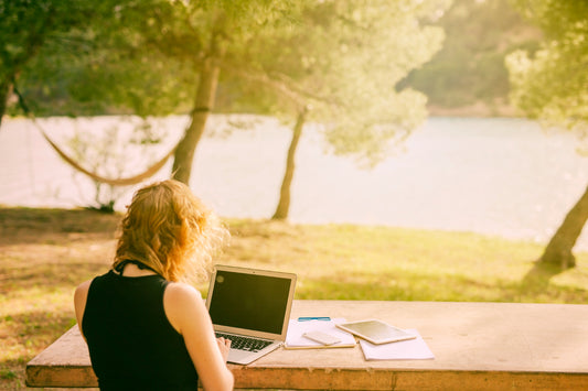Unrecognizable woman sitting at desk and working on laptop in nature
