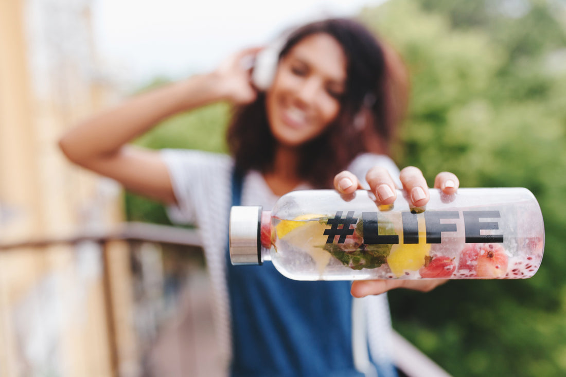 outdoor portrait of smiling black girl in white shirt with bottle in her hand on foreground