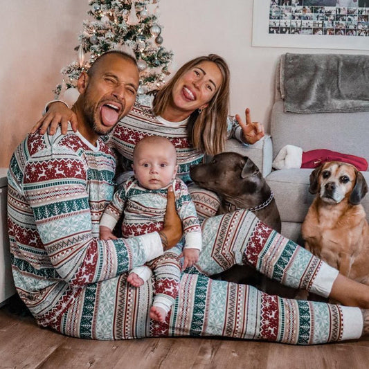 Family in matching pajamas with two dogs in a living room decorated for Christmas.